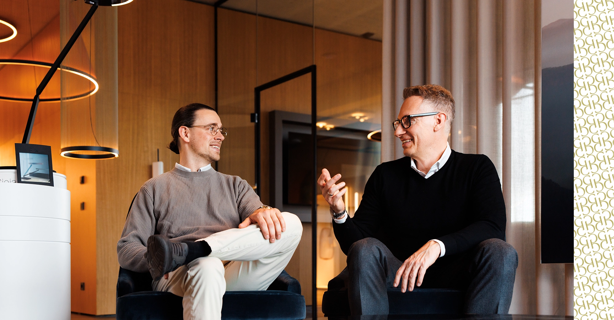 Georg und Roman sitzen nebeneinander und lächeln sich an
